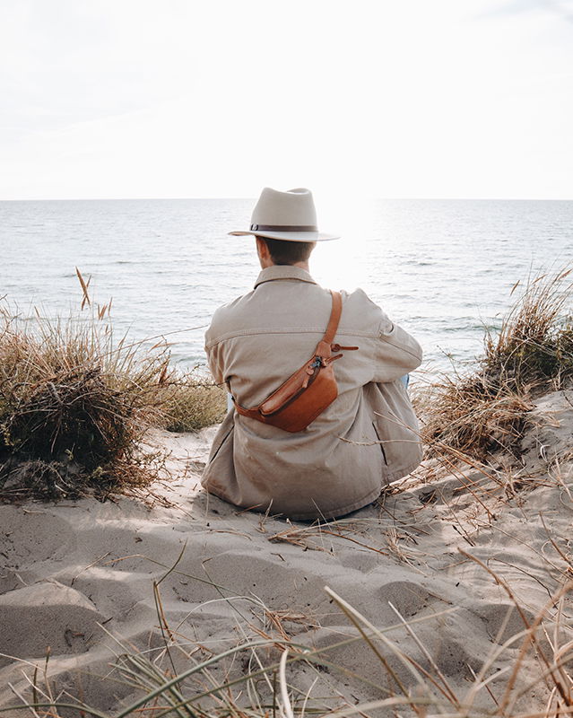 männliches Model am Strand mit einer Herren-Gürteltasche aus Leder.